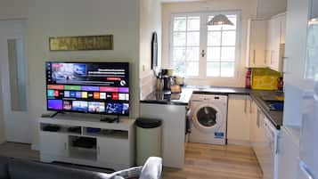 A modern kitchen with a washing machine, a dining area with a sofa, and a television displaying a website.