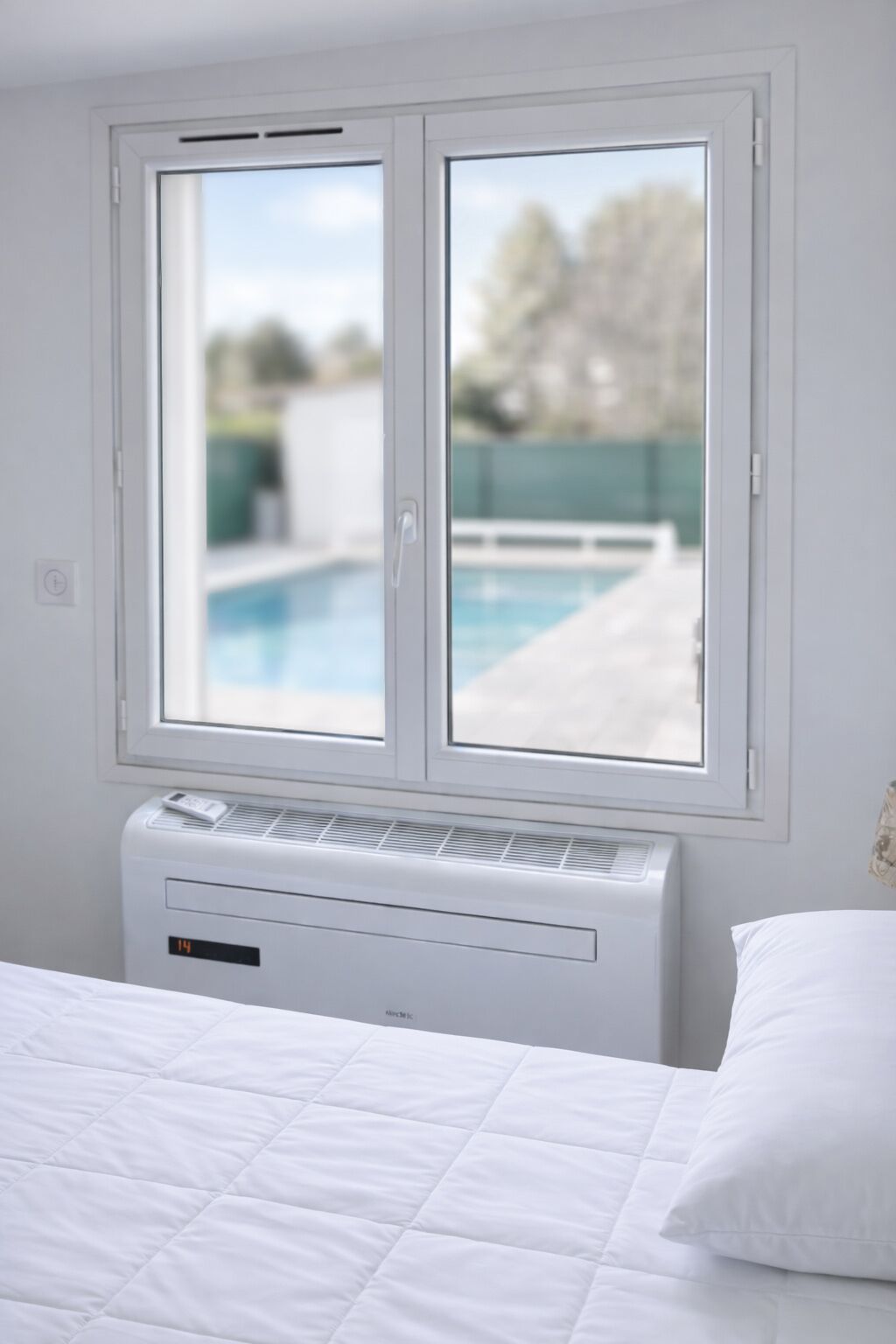 Une chambre à coucher avec un lit, une fenêtre donnant sur une piscine et un climatiseur fixé au mur.