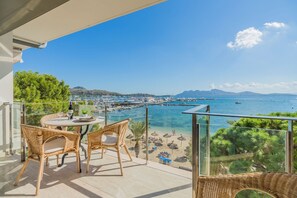 A balcony with wicker furniture, a table with a bottle and glasses, and a view of a beach and marina.