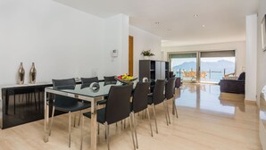 A modern dining area with a glass table and chairs, a black cabinet, and a view of the sea through large windows. - Apartment Colorado 3B By SunVillas Mallorca (Port de Pollensa)