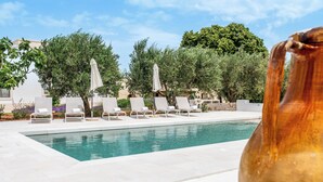 A pool area with lounge chairs and umbrellas, surrounded by trees and a stone building.