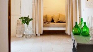 A cozy room with a stone archway, a bed with yellow pillows, a hanging lamp, and a table with green vases.