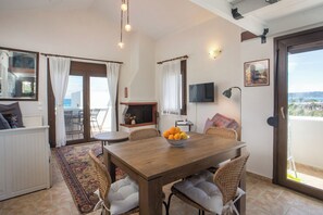 Un coin repas avec une table en bois, des chaises en osier, un panier de fruits et un téléviseur fixé au mur.