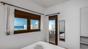 Ein Schlafzimmer mit Bett, einem Fenster mit Vorhängen, einem Balkon mit einem Stuhl und einem Spiegel.