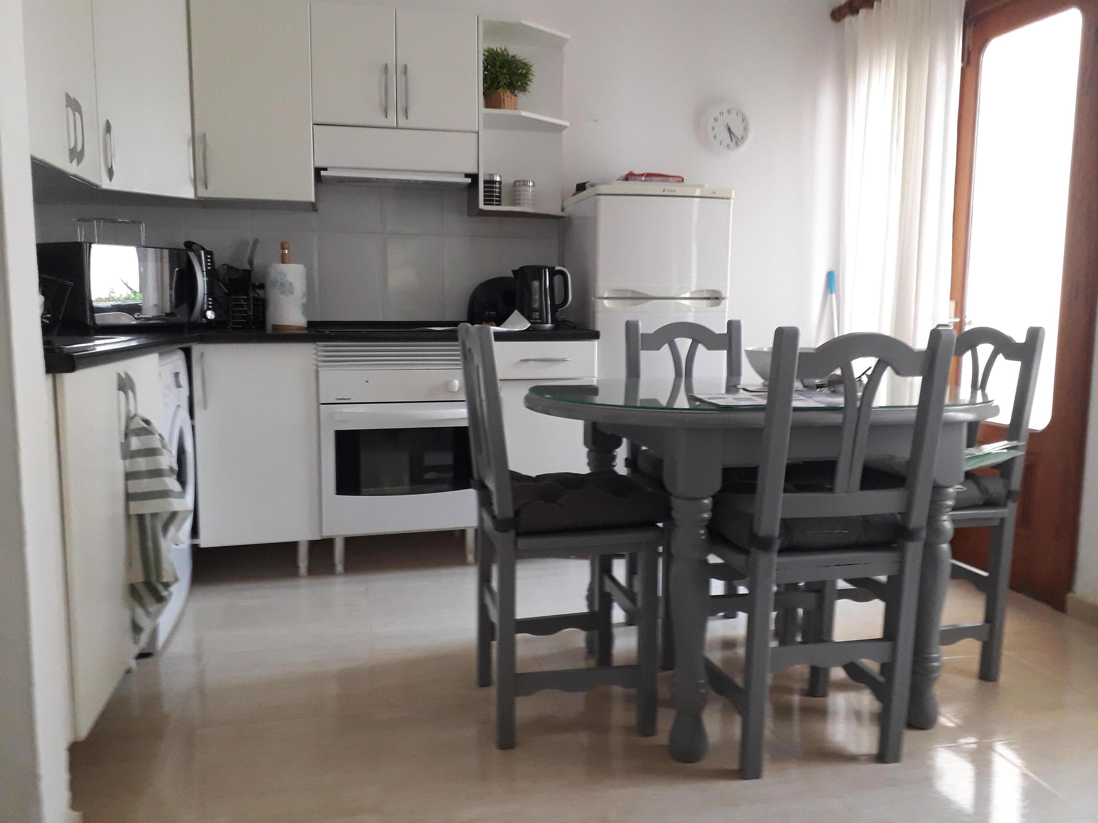 A compact kitchen with white cabinets, a microwave, a stove, and a refrigerator. There is a dining table with four chairs.