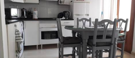 A compact kitchen with white cabinets, a microwave, a stove, and a refrigerator. There is a dining table with four chairs.