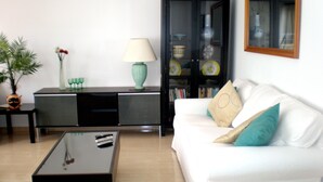 A living room with a white sofa, a black coffee table, a teal lamp, a black cabinet, and a bookshelf. - 2 Bed Ground Floor in small complex and close to all amenities 1 minute seafront (Puerto del Carmen)