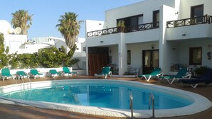 A swimming pool with lounge chairs and a building with balconies. - 2 Bed Ground Floor in small complex and close to all amenities 1 minute seafront (Puerto del Carmen)
