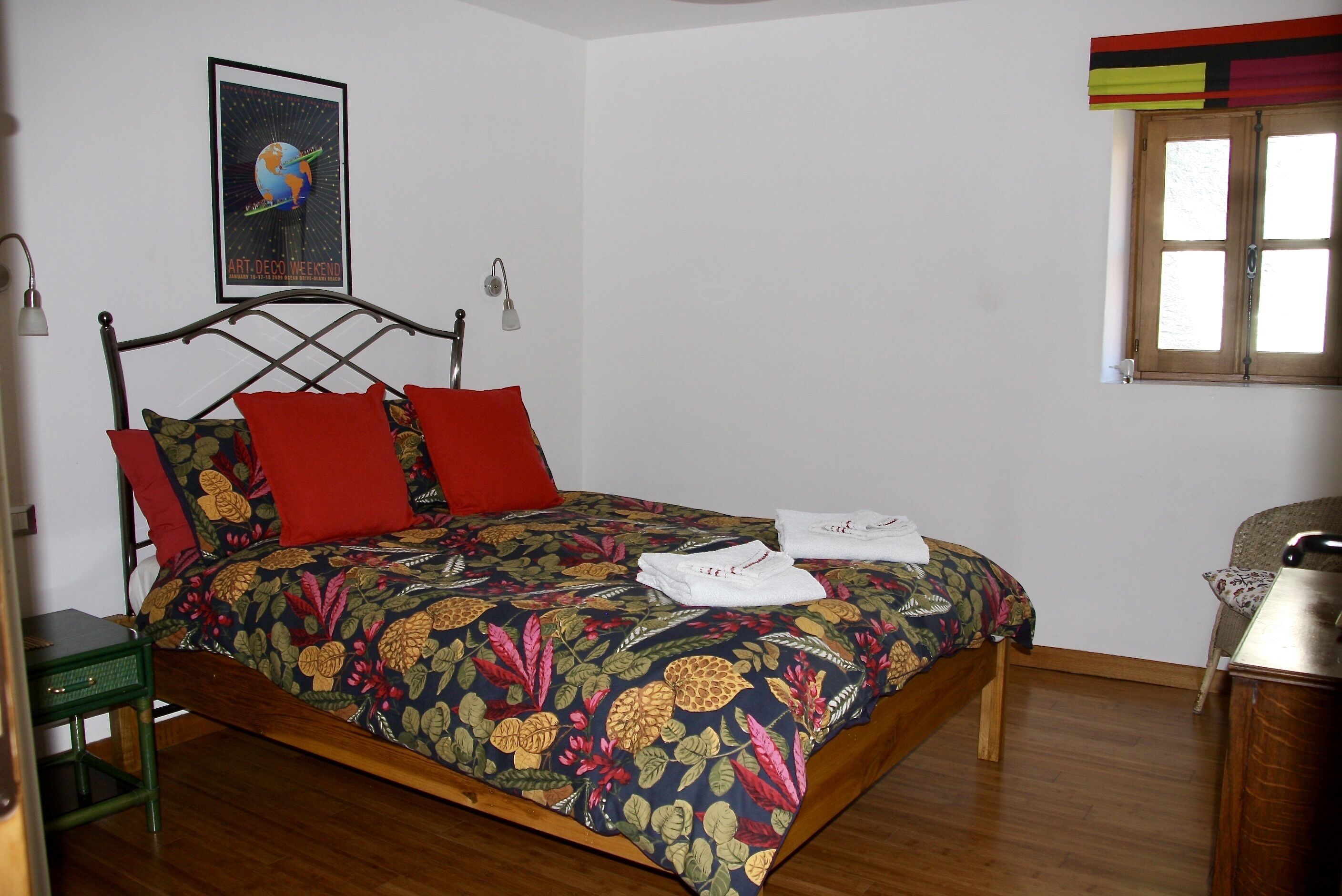 Ein Bett mit blumigem Überwurf, roten Kissen und einem Bild an der Wand.