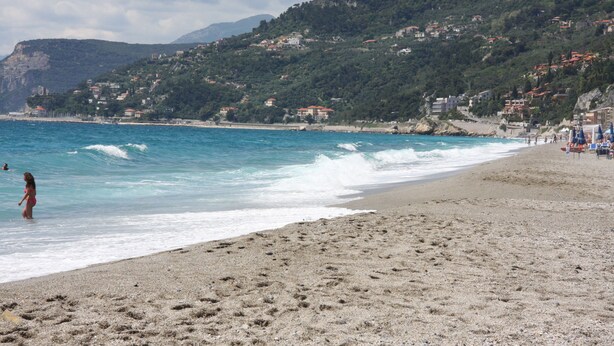 A beach with clear blue water, a sandy shore, and buildings on a hillside in the background. - Charming House in an Authentic Italian Mountain Village (Rezzo)