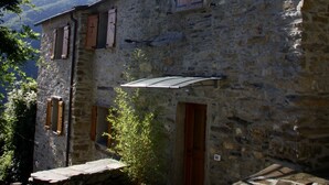 A stone building with wooden shutters and a small garden area. - Charming House in an Authentic Italian Mountain Village (Rezzo)