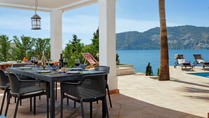 An outdoor dining area with a table set for a meal, overlooking a body of water and hills.