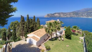 A coastal property with a stone terrace, palm trees, and a view of the sea.