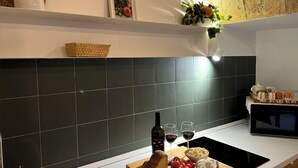 Une cuisine moderne avec un dosseret de carreaux noirs, un plan de travail blanc, une miche de pain, des tomates, un bol de fromage et une bouteille de vin.