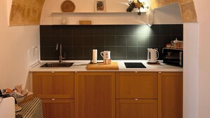 Une cuisine dotée d’une arche en pierre, de carreaux noirs, de meubles en bois, d’un évier et d’un plan de travail sur lequel se trouvent une bouilloire et une tasse.