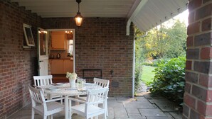 A covered patio with a brick wall, a white table with chairs, and a hanging light fixture. - Private, spacious, elegant flat with lovely views, in a beautiful area (Westcott)