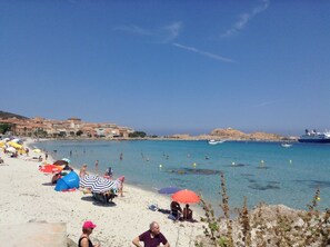 Una playa con gente, sombrillas y barcos.
