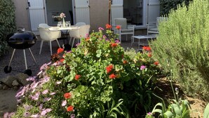 Eine Terrasse im Freien mit Grill, Esstisch, Stühlen und Sonnenschirm.