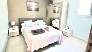 Une chambre à coucher bien rangée, avec un lit, des tables de chevet, un miroir et un tableau accroché au mur.