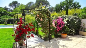 Un jardin agrémenté d’une pergola recouverte de plantes à fleurs, d’un grand pot de fleurs et d’une pelouse bien entretenue.