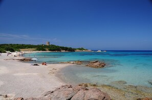 A beach with clear turquoise waters, rocky outcrops, and a tower on a hill.