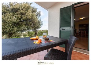 Un área de comedor al aire libre con una mesa lista para el desayuno, una silla de mimbre y vistas del paisaje circundante.