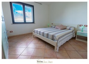 Un dormitorio con una cama, una mesita de noche, una lámpara y una ventana con vista al cielo.