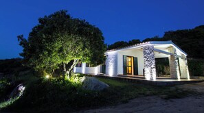 A single-story house with a stone pillar, a door with green shutters, and a tree in front. - Country holiday home - AGLIENTUHouse with garden (Aglientu)