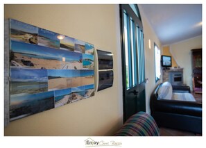 Una pared con un collage de fotografías de playa, un sofá de cuero negro y una chimenea.