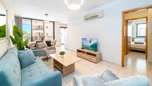 A modern living room with a sofa, coffee table, TV, and a dining area. - Oroklini - Perfectly overlooking the pool (Oroklini)