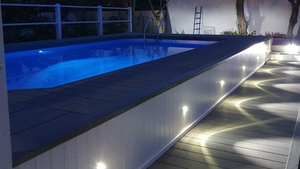 Piscina con bordo in legno e illuminazione lungo il perimetro.