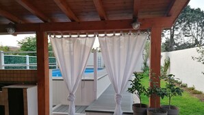 Un'area esterna coperta con piscina, piante in vaso e barbecue.