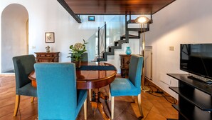 En matplats med ett runt träbord, två blå stoppade stolar, ett litet sidobord med en vas och en trappa med modern design.