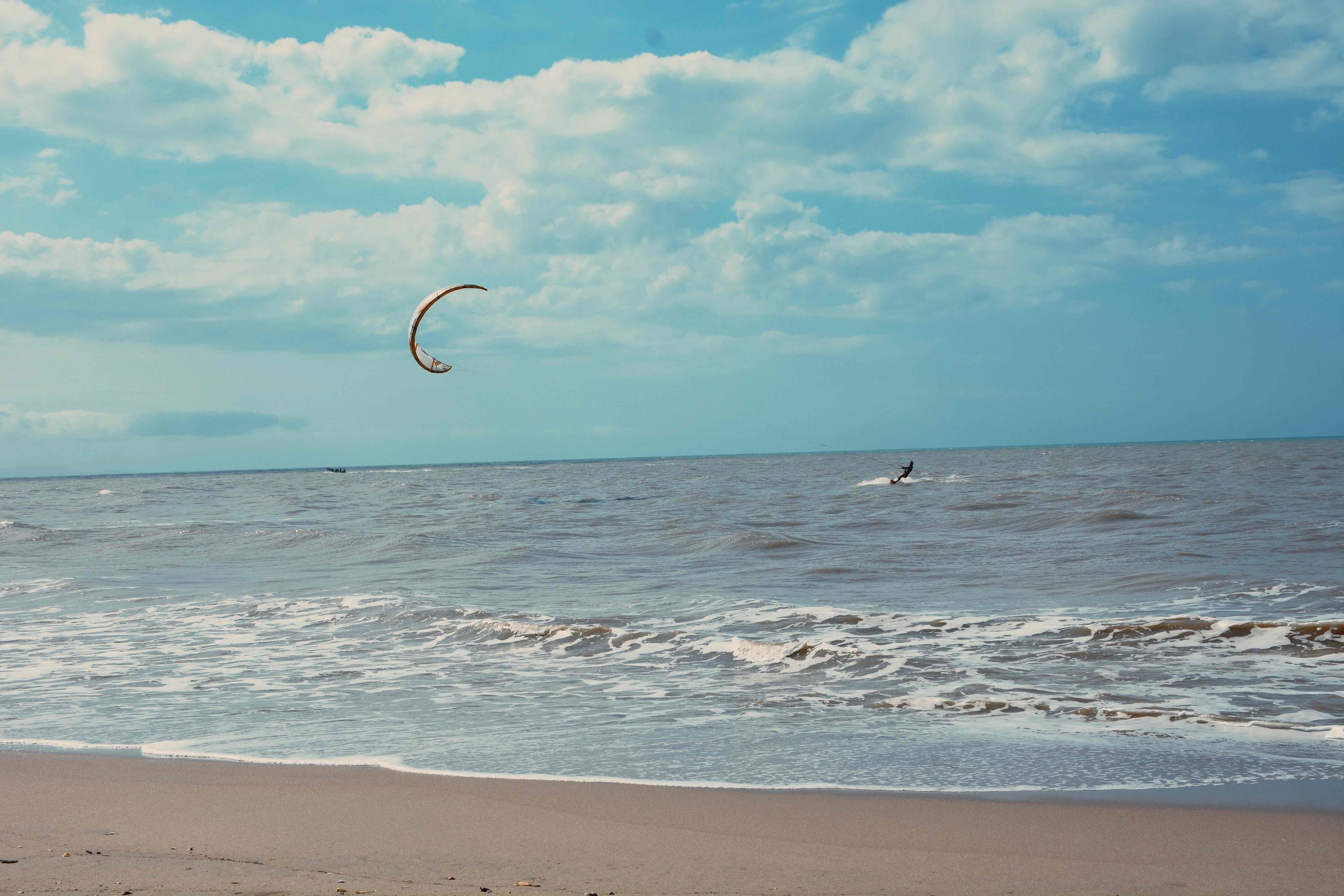 A beach with waves and a person kite surfing in the distance.