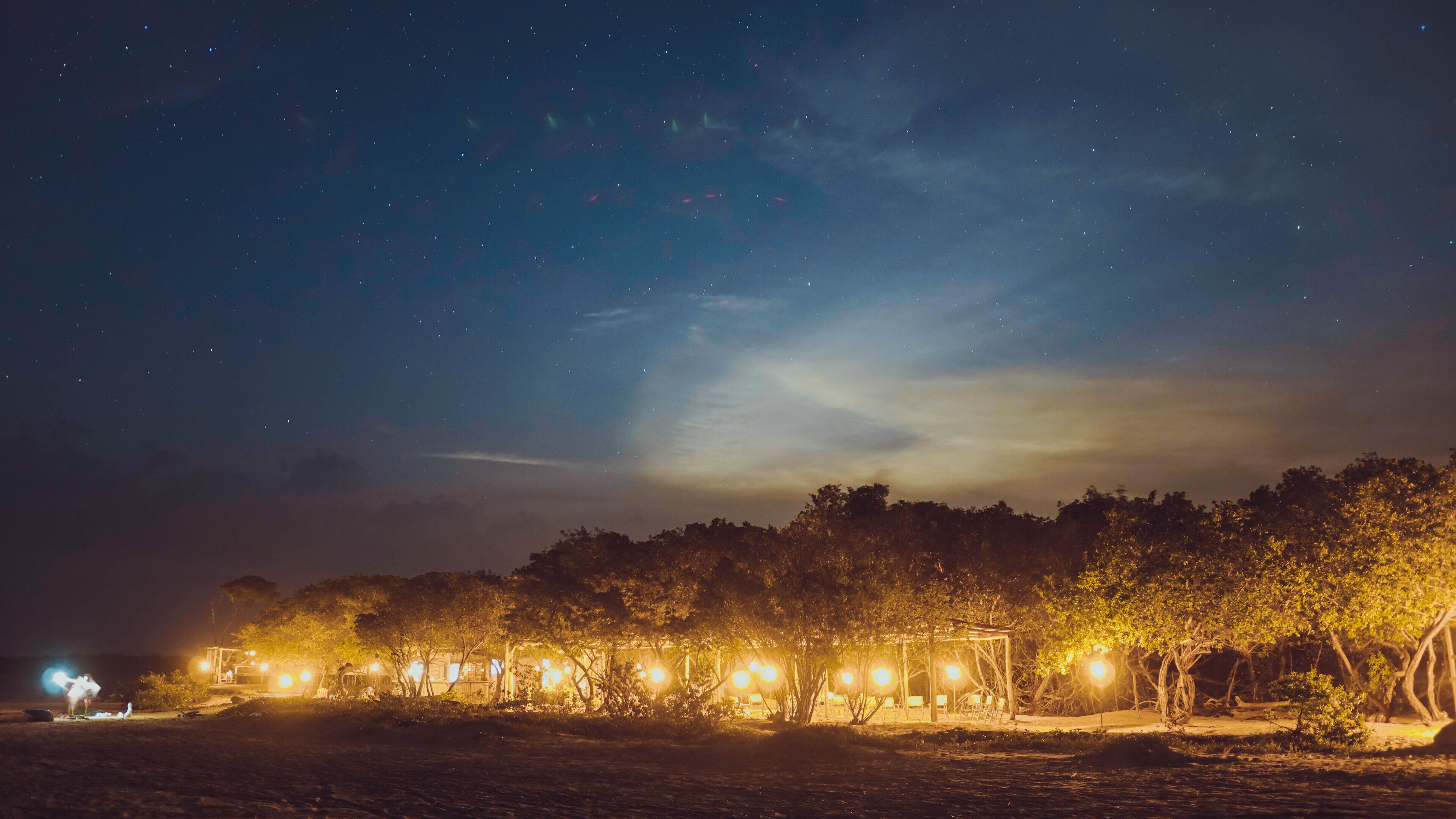 A nighttime outdoor area with trees and a gazebo under a starry sky.