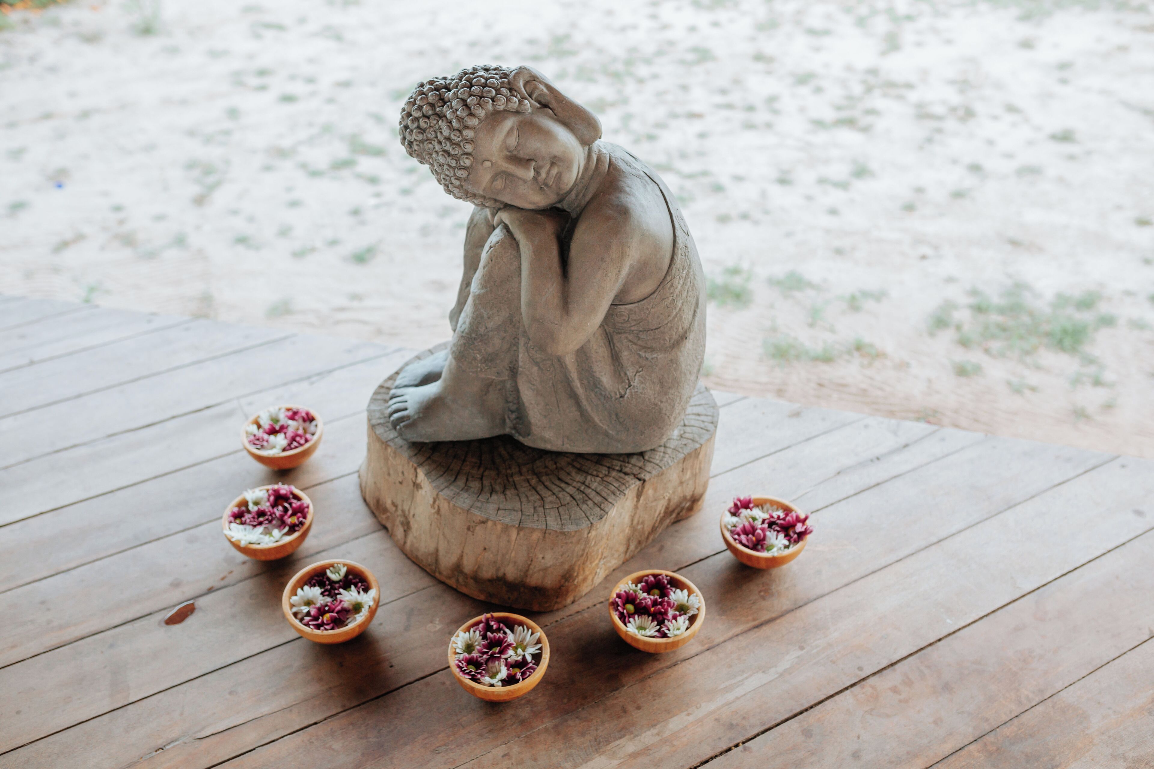 A Buddha statue on a wooden platform surrounded by small bowls of flowers.
