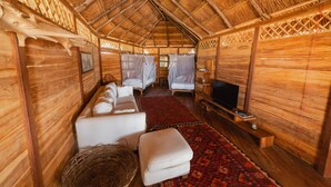 Una habitación acogedora con techo de paja, un sofá, dos camas con mosquiteras, un televisor y un tapete rojo estampado.