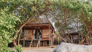 Una casa de madera con porche, rodeada de árboles y un tronco de árbol grande al frente.