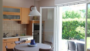 A kitchen with wooden cabinets, a built-in oven, and a dining area with a table and chairs. - Bright apartment 87 m2 near Lake Annecy (Doussard)