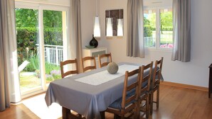 A dining area with a table set for six, wooden chairs, a vase, and a view of a garden through a sliding glass door. - Bright apartment 87 m2 near Lake Annecy (Doussard)