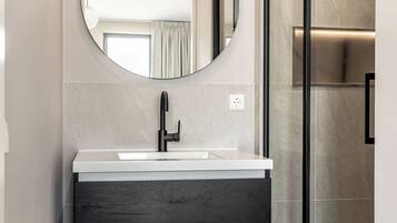 Een moderne badkamer met een ronde spiegel, een witte wastafel, donkerhouten kasten en een douchecabine met glazen wanden.