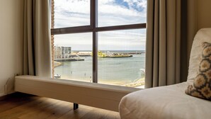 A room with a large window, a bed, and a view of a waterfront with buildings and docks. - BizStay Harbour Scheveningen Apartments (The Hague)