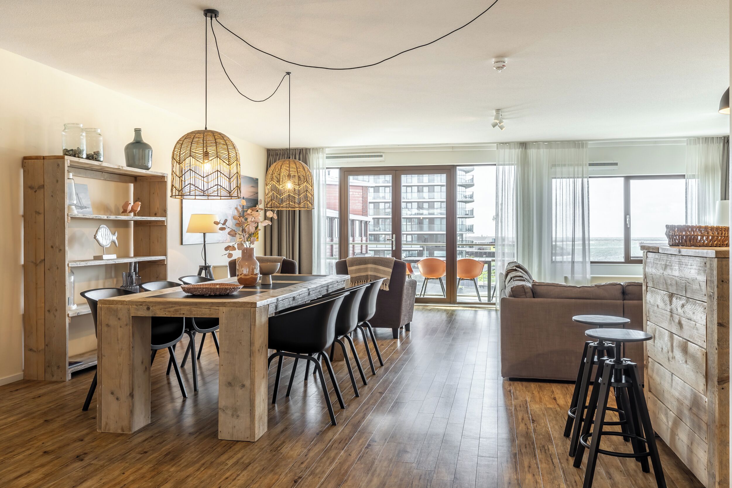 A modern kitchen with a wooden island, black bar stools, and a dining area with a large window offering a city view.