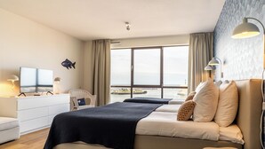 A hotel room with a bed, a television, a desk, and a view of the sea. - BizStay Harbour Scheveningen Apartments (The Hague)
