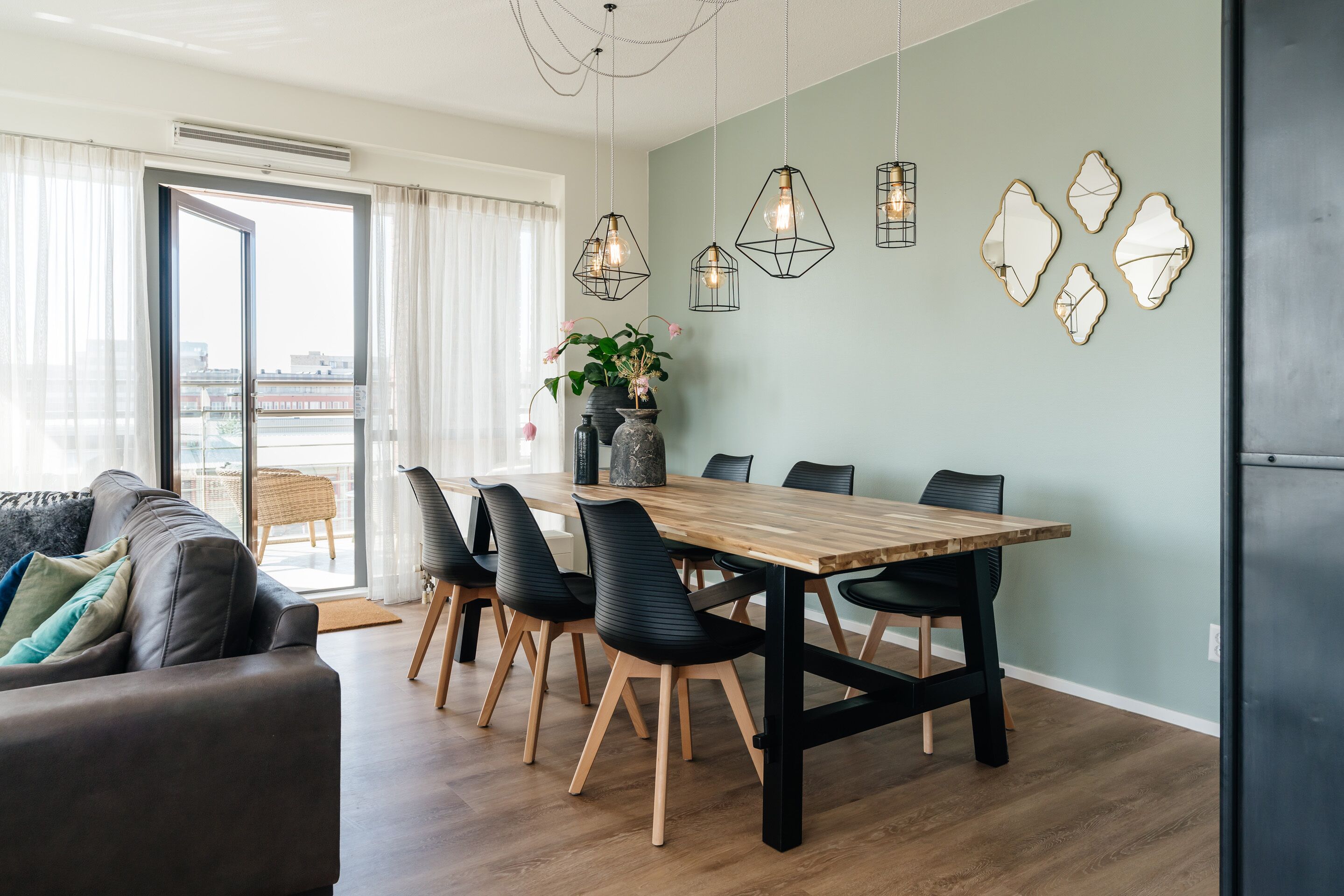 Uma sala de estar moderna com uma mesa de jantar de madeira, cadeiras pretas e um sofá cinza.