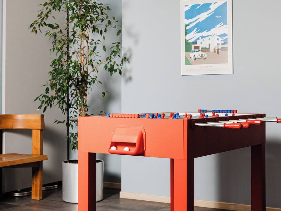 Una habitación con una mesa de fútbol de mesa, una silla de madera y una planta en maceta.