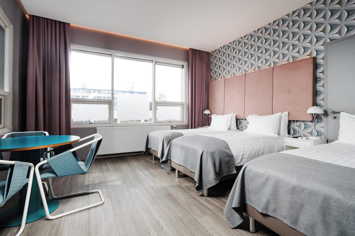 Una habitación de hotel con dos camas, una mesa de comedor con sillas y un ventanal amplio.