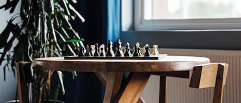 Una mesa de madera para jugar al ajedrez con sillas, una planta en maceta y una ventana al fondo.