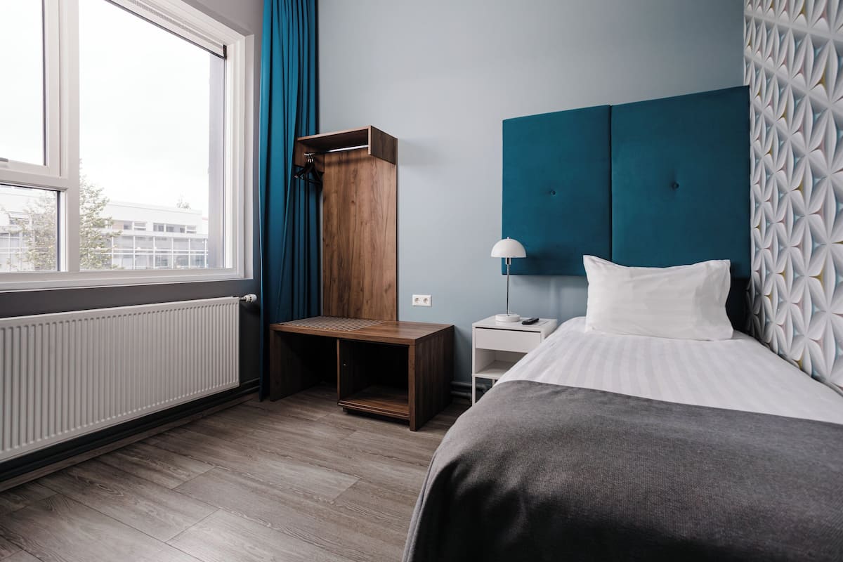 Una habitación de hotel moderna con una cama grande, un armario de madera, una mesita de noche y vistas al exterior.
