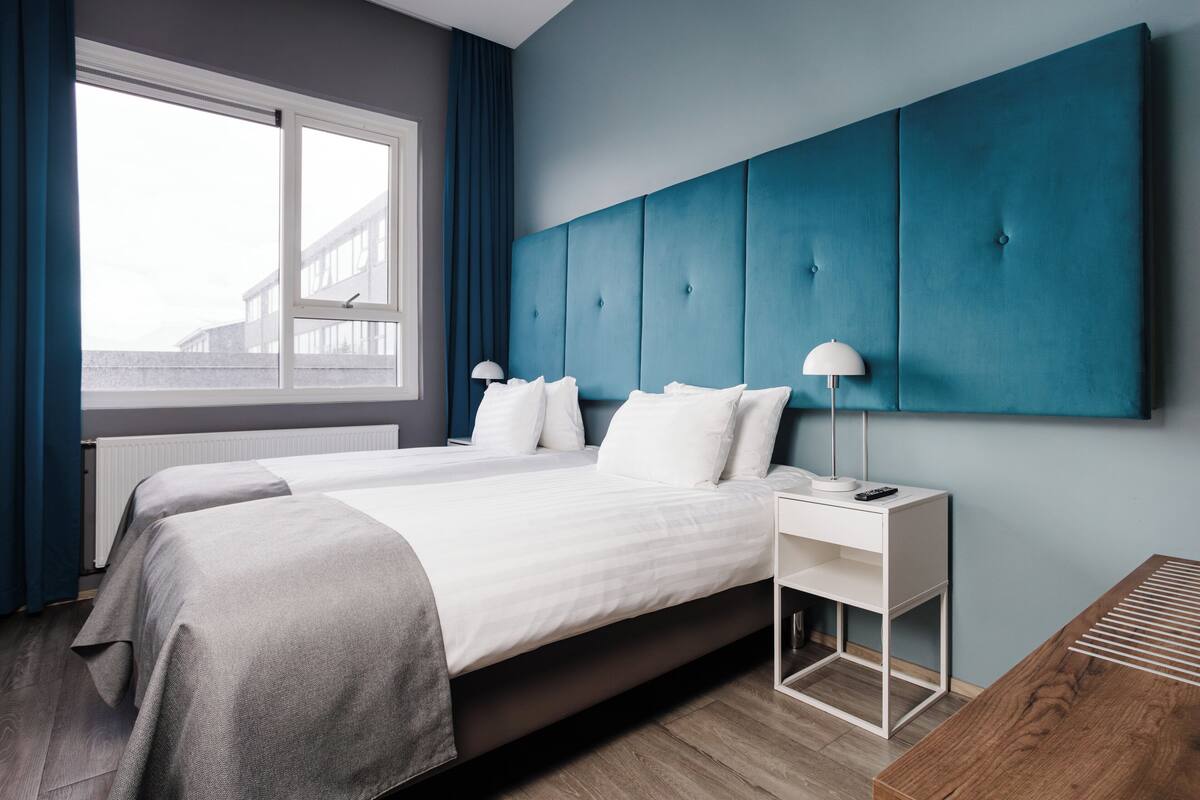 Una habitación de hotel moderna con una cama grande, una mesita de noche y vistas a un edificio.